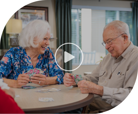 A video of an elderly man and woman sitting at a table, smiling and playing cards together.