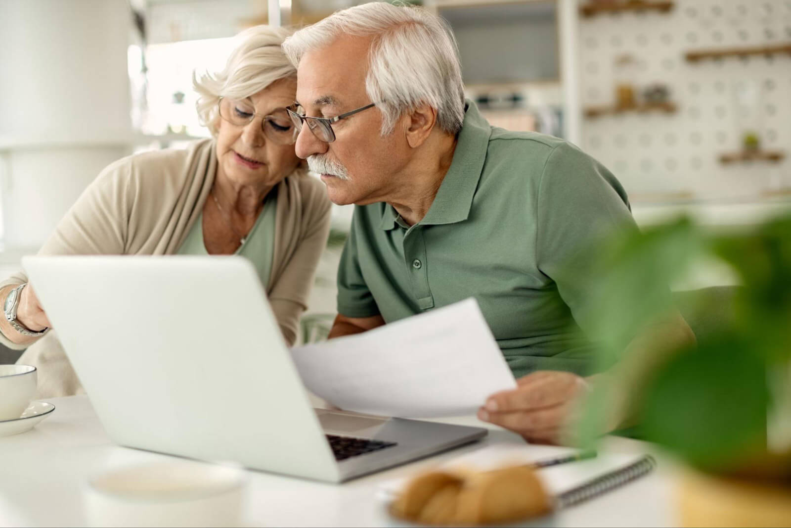 An older couple reviews documents together on a laptop at home, representing financial awareness, online safety, and protecting seniors from scams.