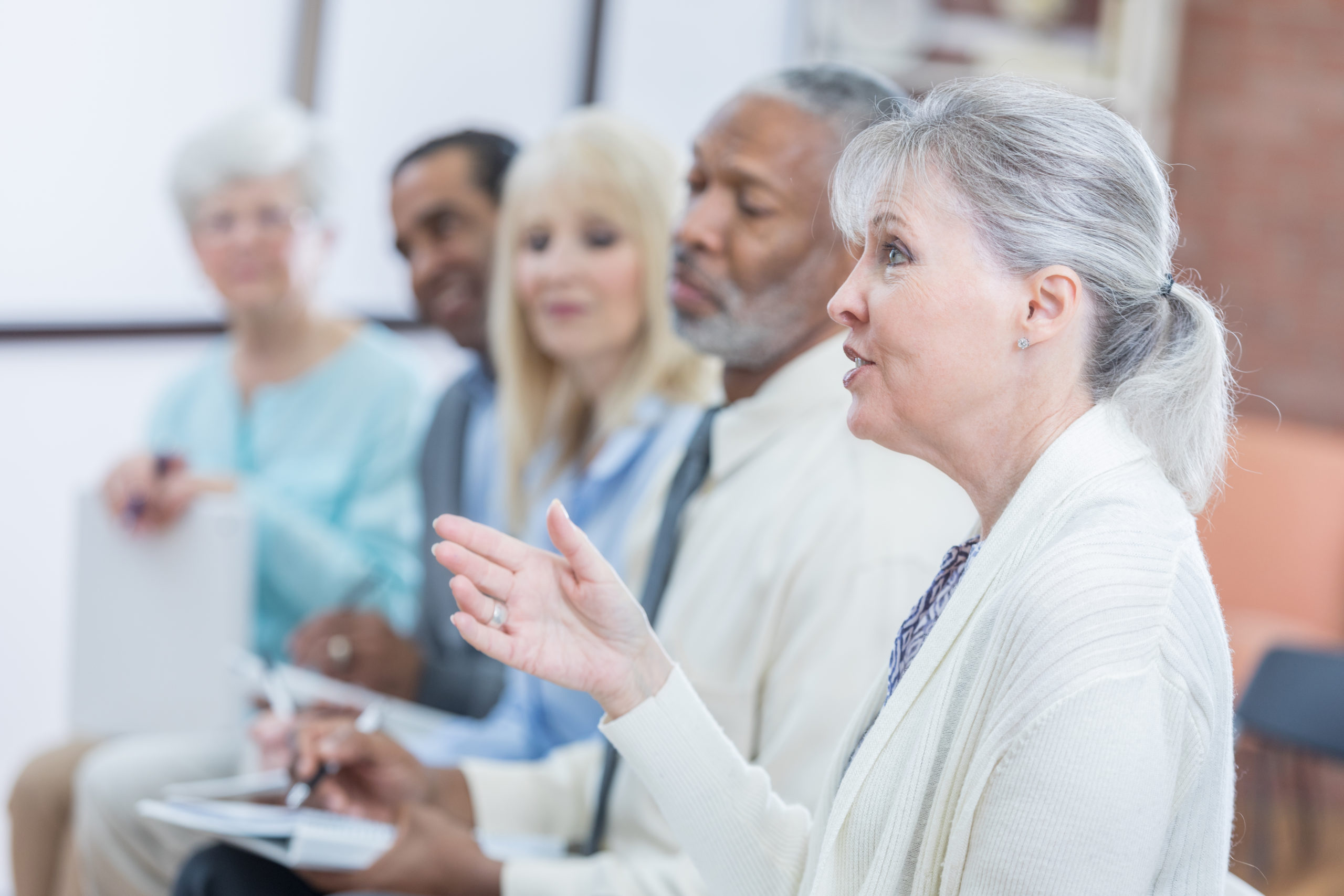 Senior woman gestures while asking question during continuing education class